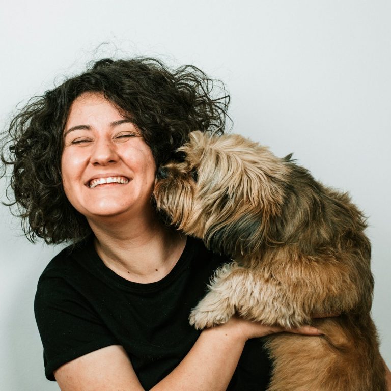 Auf dem Arm Lächelnde Person mit lockigem Haar, die einen Hund im Arm hat.